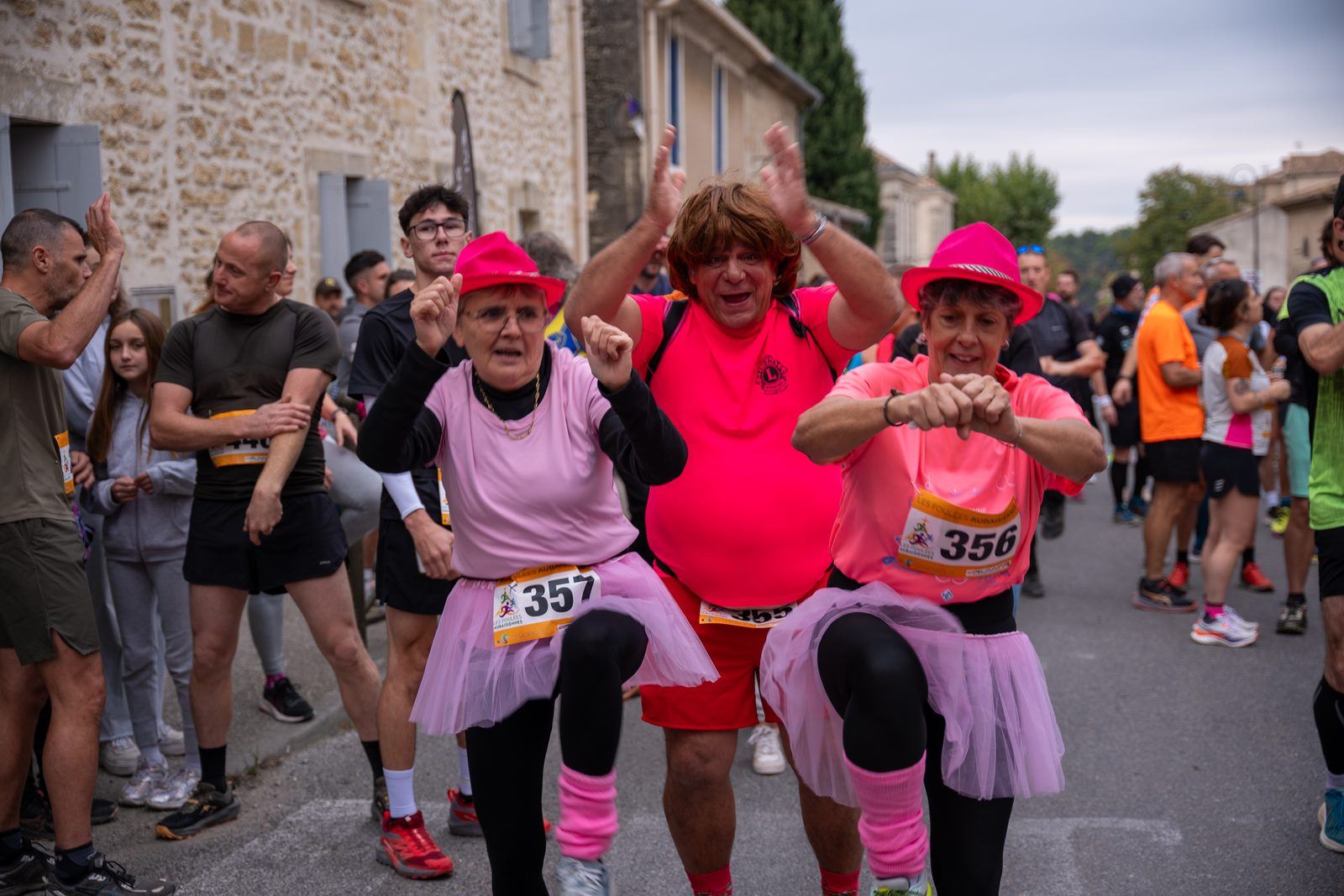 Trois participants déguisés en rose, chapeau et tutu, s'échauffent en riant au milieu du peloton.