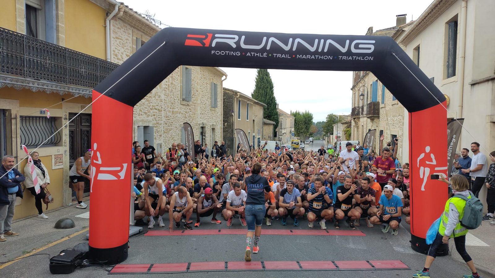 Le peloton accroupi sous l'arche de départ, dans une rue du village bordée de maisons en pierre.