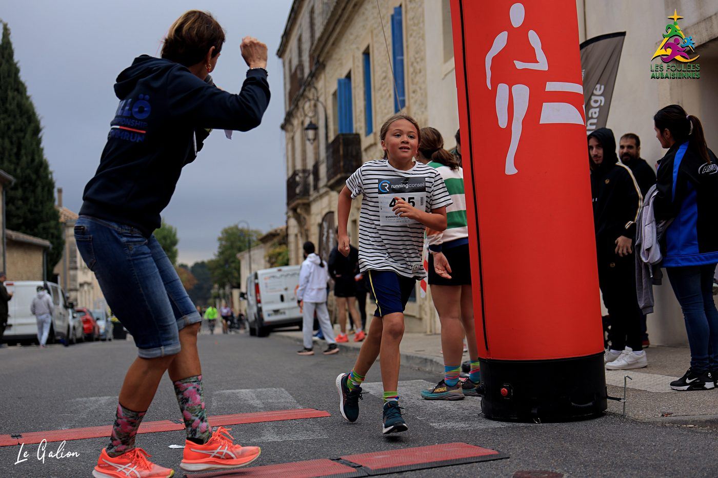 Une bénévole encourage une jeune coureuse qui franchit la ligne d'arrivée.
